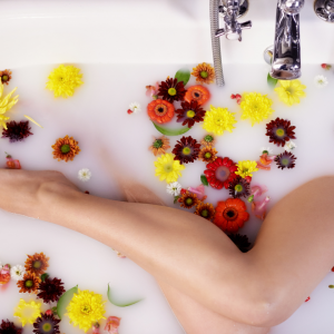 a woman in a milk bath with orange, red and yellow flowers to represent loving yourself