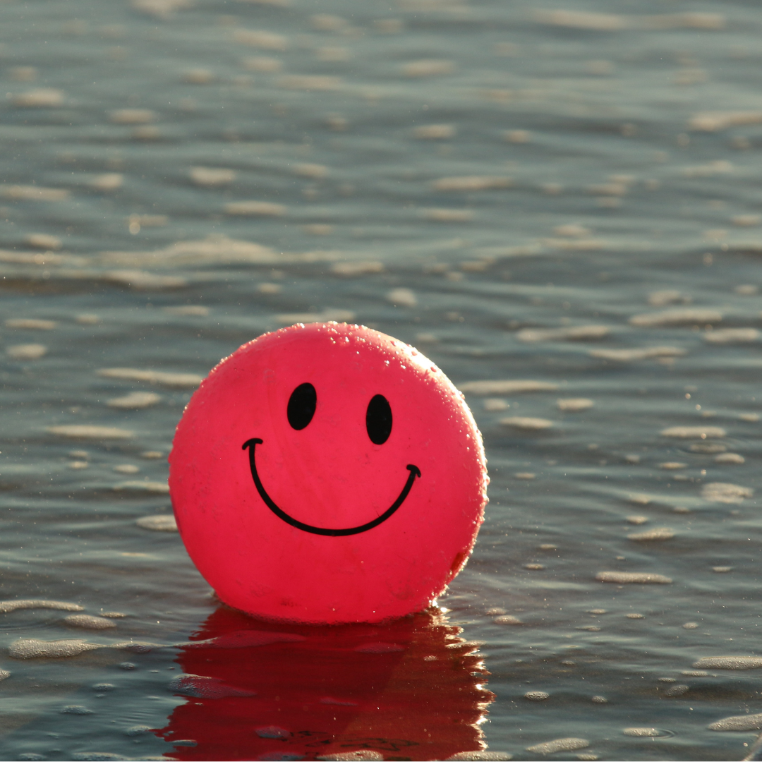 a red smiley face beach ball floating on the water at sunset